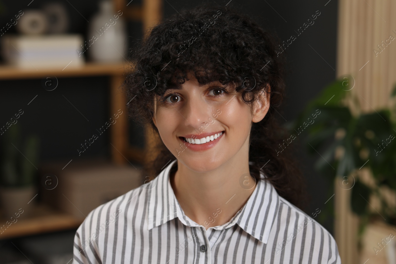 Photo of Portrait of beautiful woman with curly hair indoors. Attractive lady smiling and looking into camera