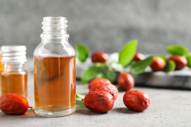 Photo of Glass bottle with jojoba oil and seeds on grey stone table. Space for text