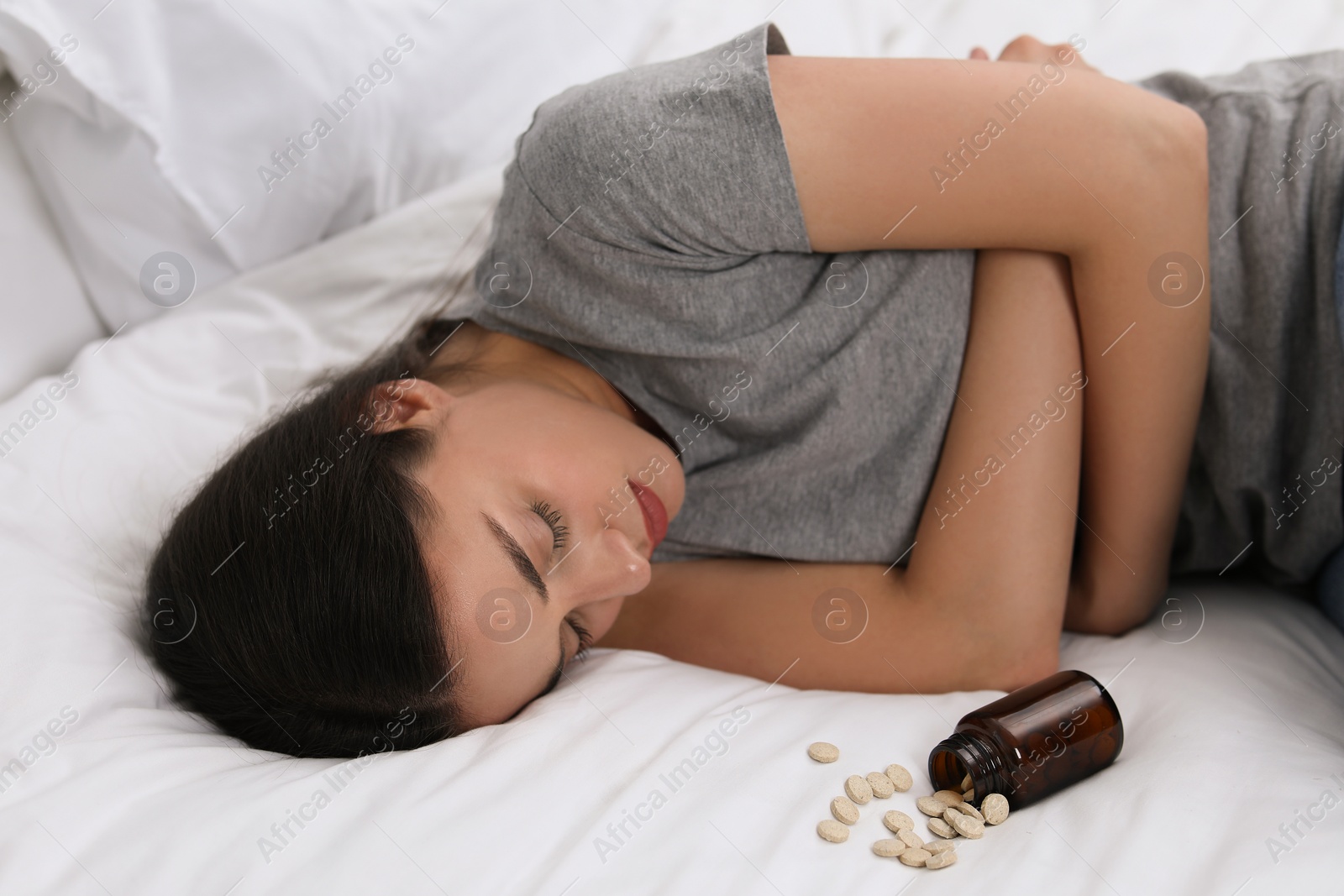 Photo of Woman sleeping on bed near overturned bottle with antidepressants