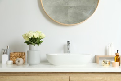 Photo of Vase with beautiful white roses and toiletries near sink in bathroom