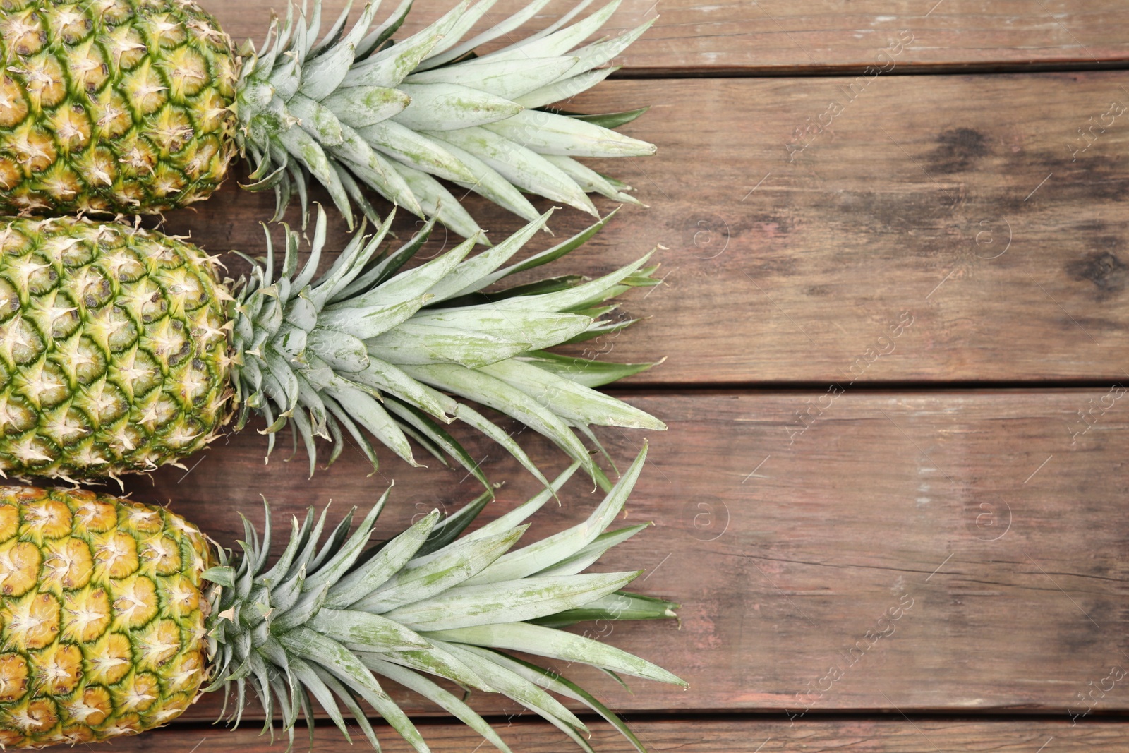 Photo of Delicious ripe pineapples on wooden table, flat lay. Space for text