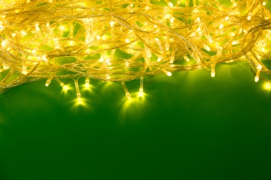 Glowing Christmas lights on green background, top view. Space for text