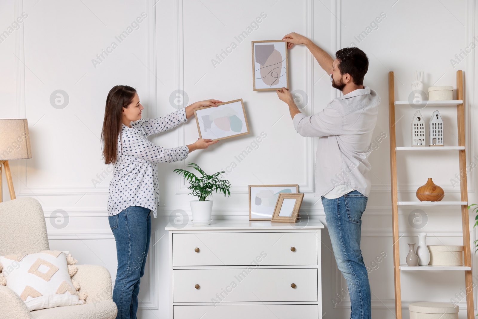 Photo of Man and woman hanging picture frames on white wall at home