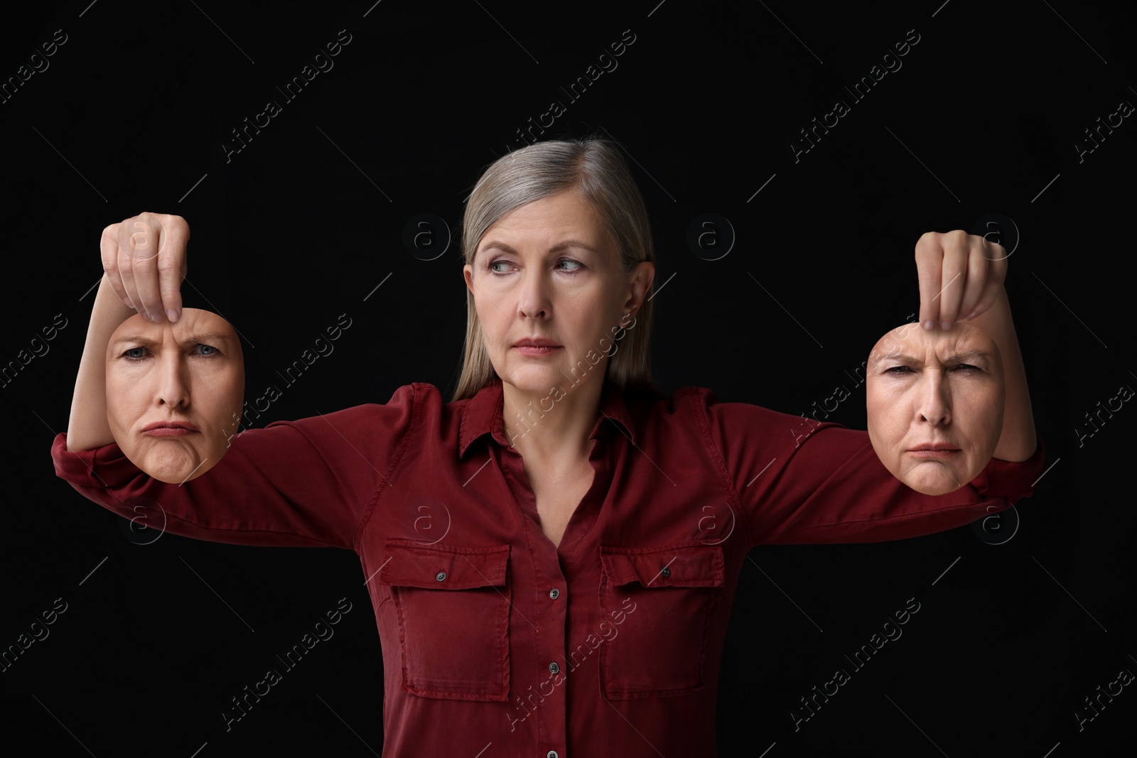 Image of Mature woman holding masks with his face showing different emotions on black background. Balanced personality