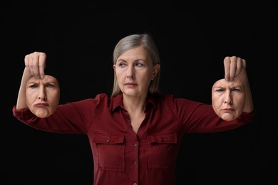 Mature woman holding masks with his face showing different emotions on black background. Balanced personality