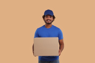 Photo of Happy young courier with parcel on light brown background
