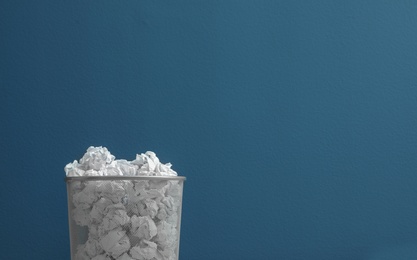 Photo of Metal bin with crumpled paper against color background. Space for text