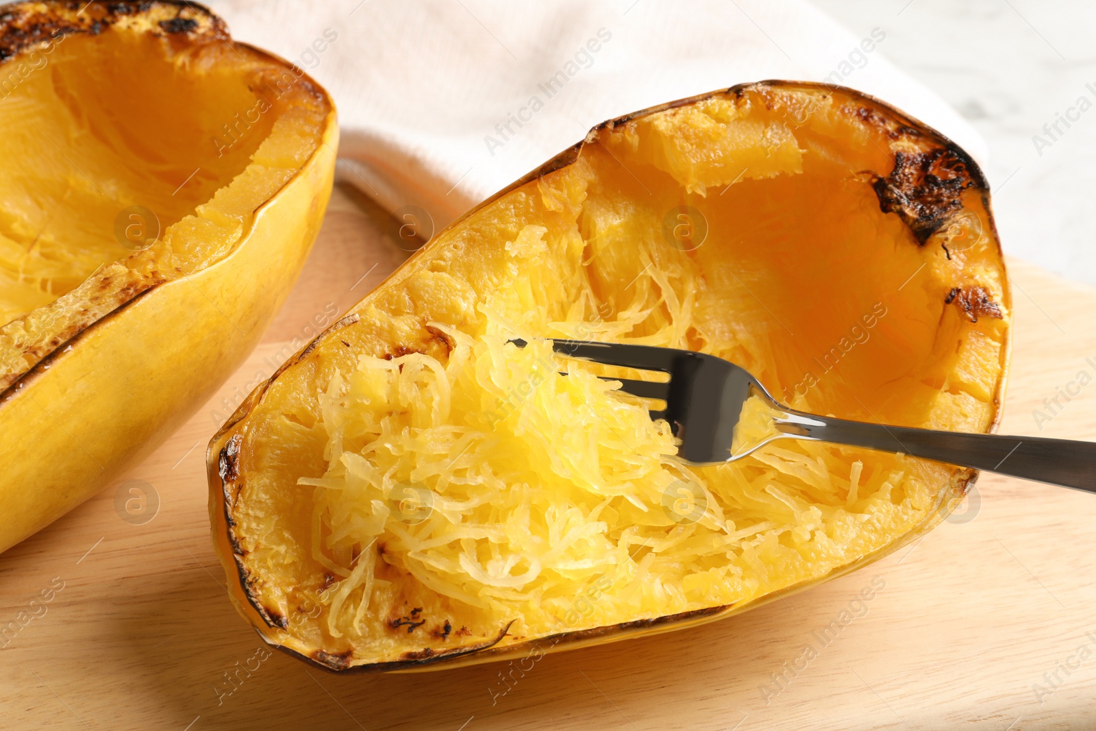 Photo of Wooden board with cooked spaghetti squash and fork on table, closeup