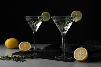 Photo of Martini glasses of refreshing cocktail decorated with lemon slices and rosemary on grey textured table