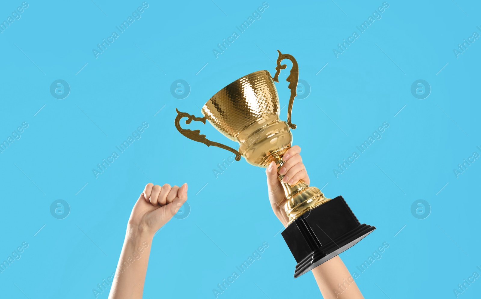 Photo of Woman holding gold trophy cup on light blue background, closeup