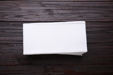 Photo of Stack of clean tissue towels on wooden table, top view