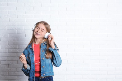 Photo of Teen girl listening to music with headphones near brick wall. Space for text