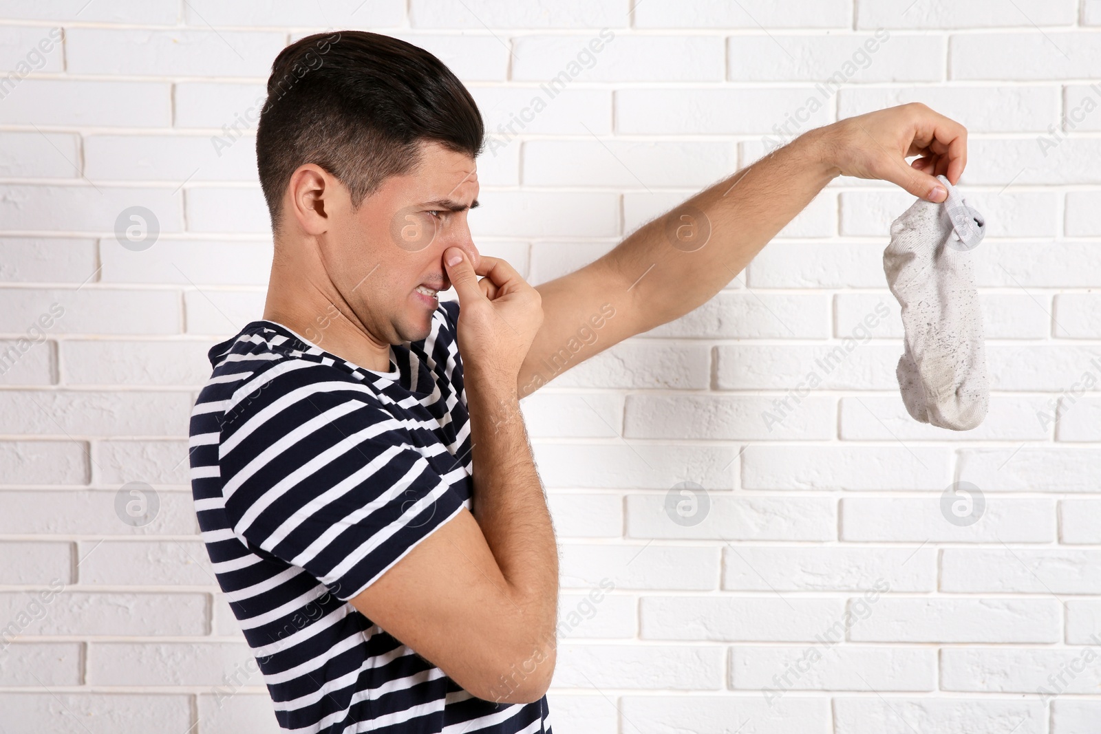 Photo of Man feeling bad smell from dirty socks near white brick wall