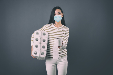 Image of Woman in medical mask holding toilet paper rolls on grey background