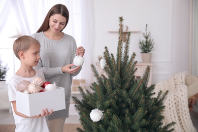 Photo of Happy mother with her cute son decorating Christmas tree together at home