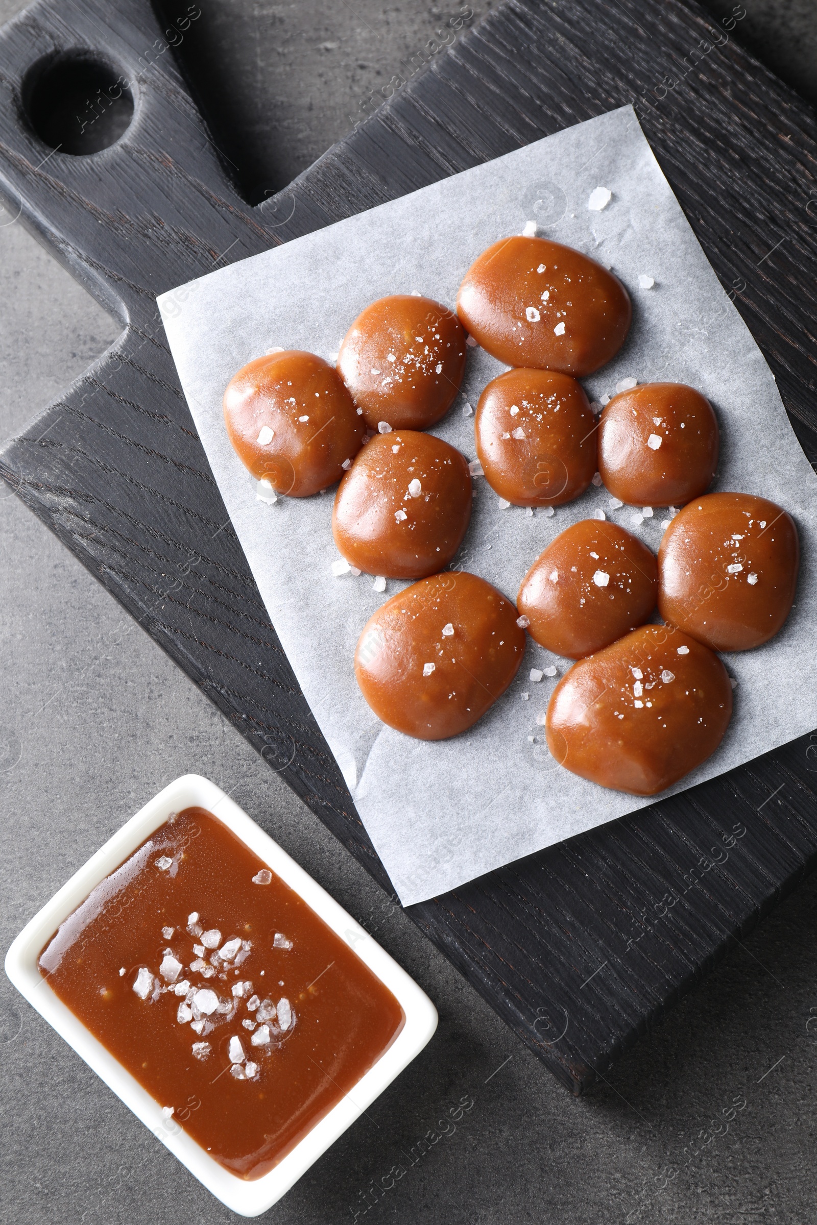 Photo of Tasty candies, caramel sauce and salt on grey table, top view