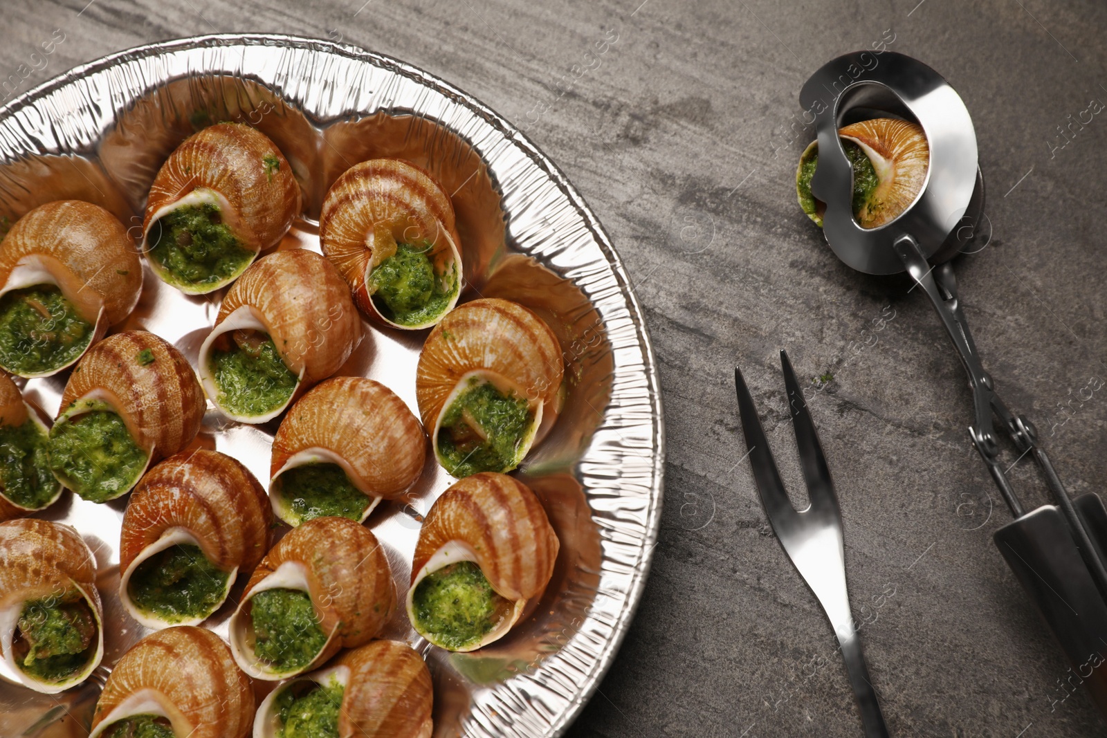 Photo of Delicious cooked snails served on grey table, flat lay