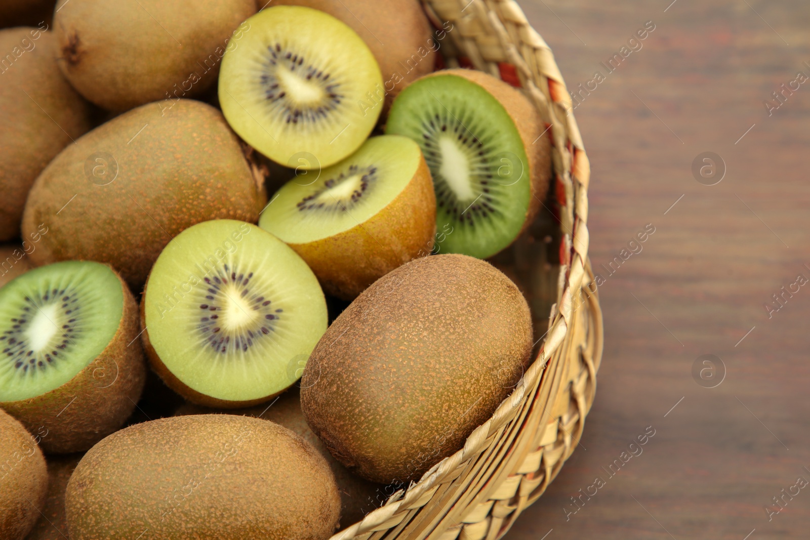 Photo of Basket of many whole and cut fresh kiwis on wooden table, closeup