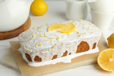 Photo of Tasty lemon cake with glaze and citrus fruits on white wooden table, closeup