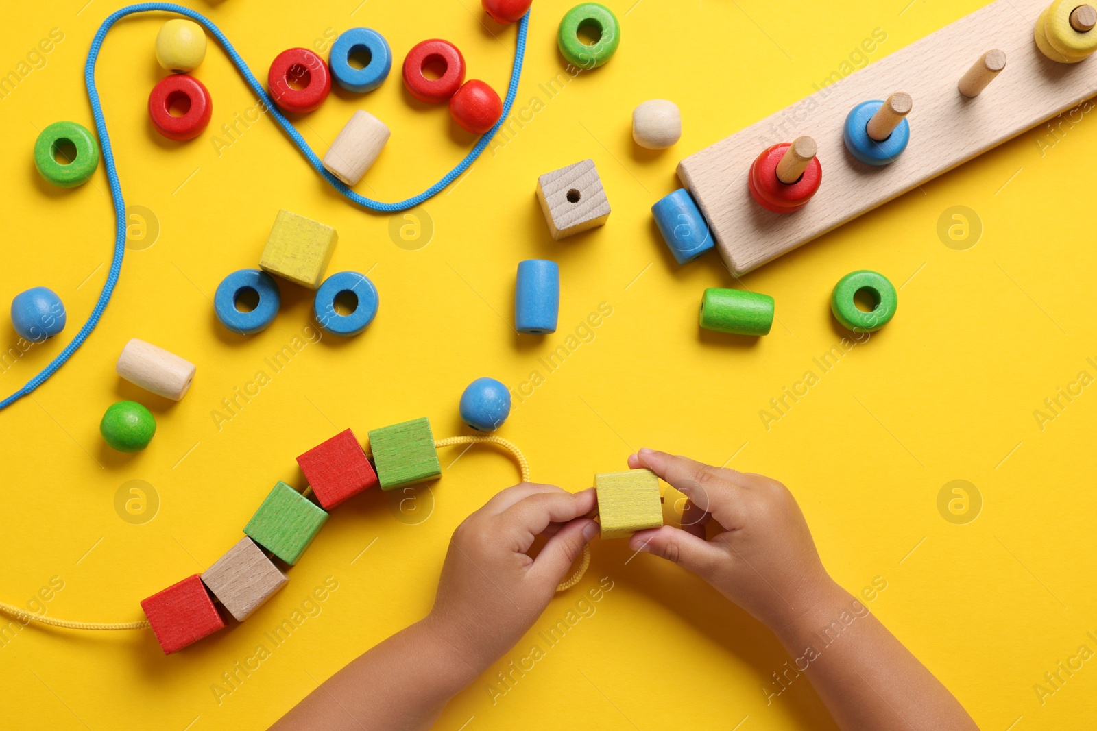 Photo of Motor skills development. Little child playing with wooden pieces and string for threading activity at yellow table, top view