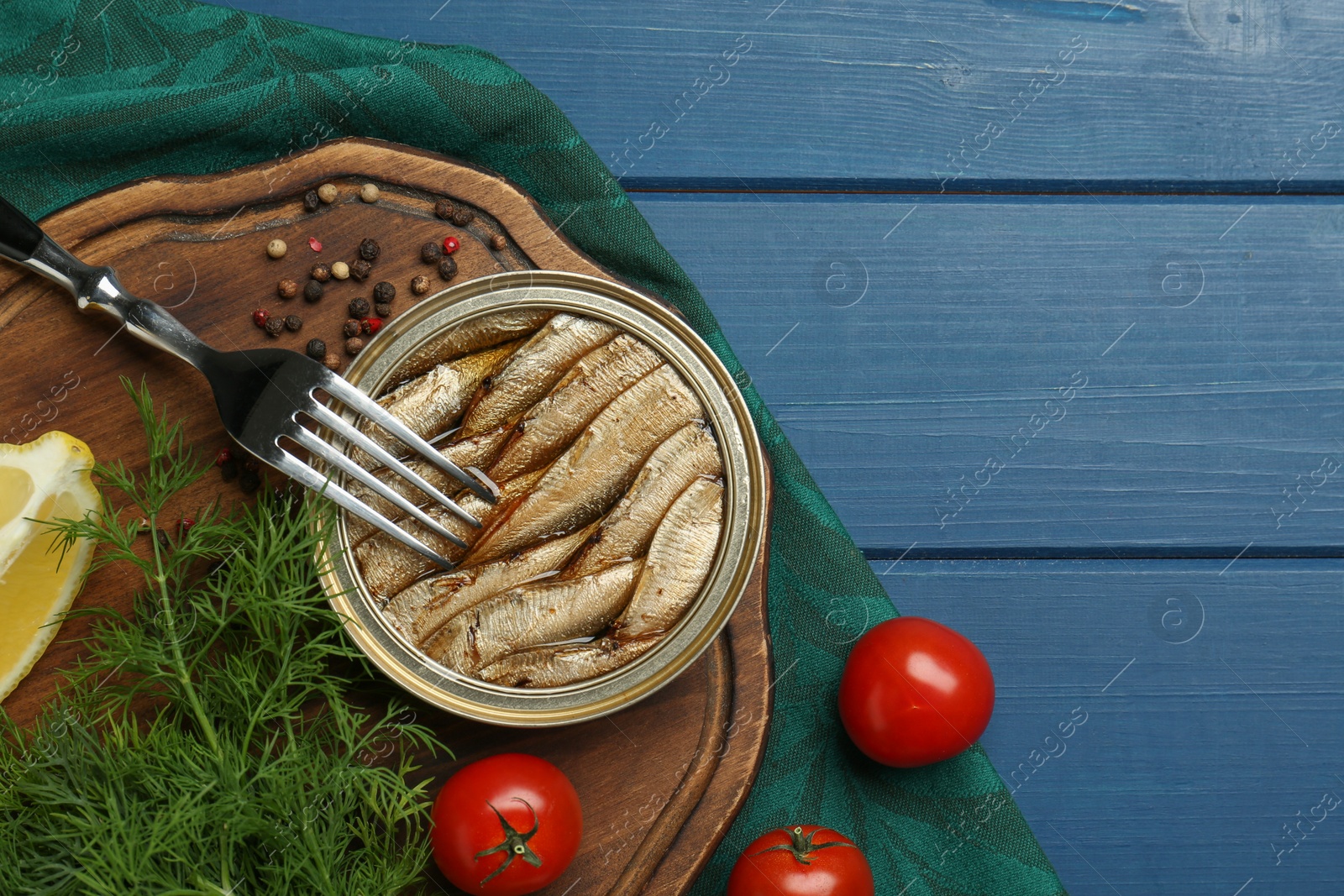 Photo of Tin can with tasty sprats served on blue wooden table, flat lay. Space for text