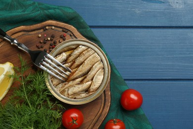 Tin can with tasty sprats served on blue wooden table, flat lay. Space for text