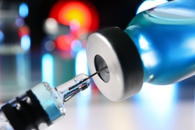 Photo of Filling syringe with vaccine from vial on blurred background, closeup
