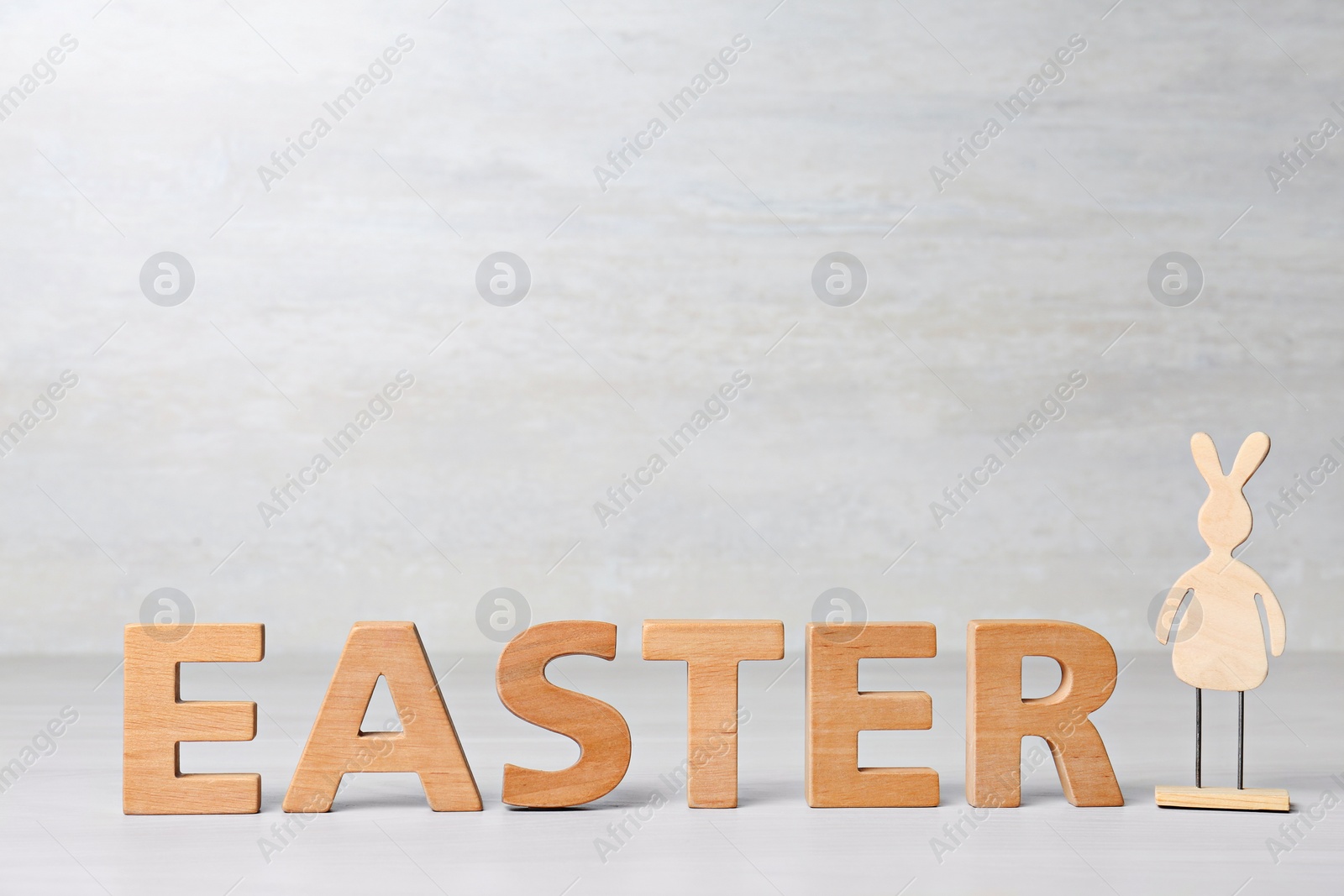 Photo of Word EASTER made of wooden letters and decorative bunny on table against light background