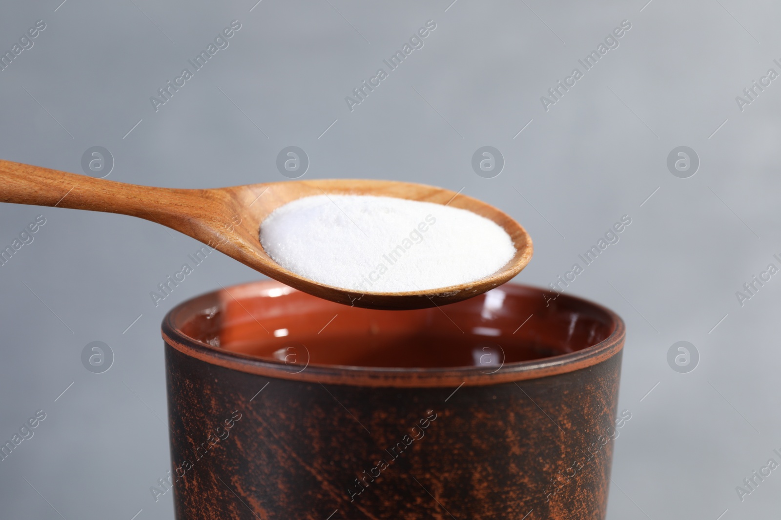 Photo of Spoon with baking soda over glass of water on grey background, closeup