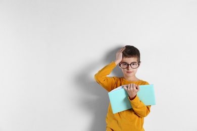 Cute little boy with book on light background, space for text