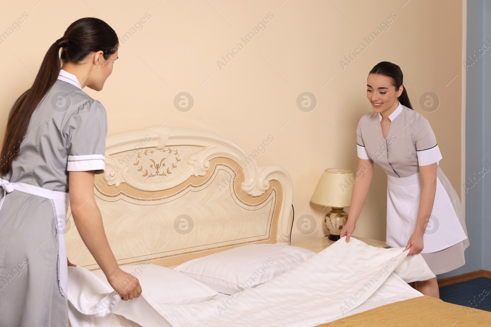 Photo of Young chambermaids making bed in hotel room