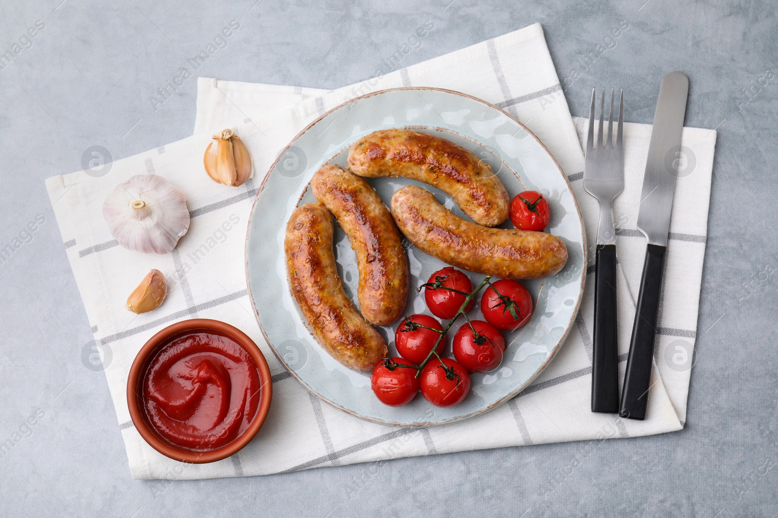 Photo of Tasty homemade sausages, tomatoes, garlic and ketchup on grey textured table, flat lay