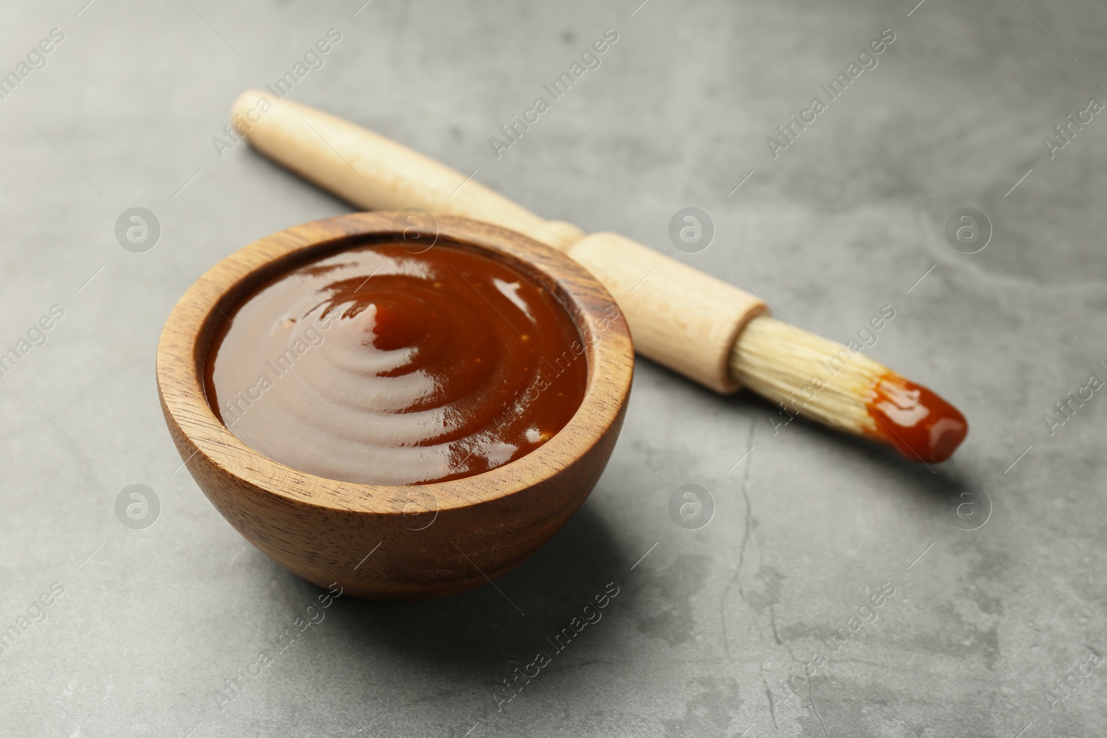 Photo of Tasty barbeque sauce in bowl and brush on grey textured table, closeup