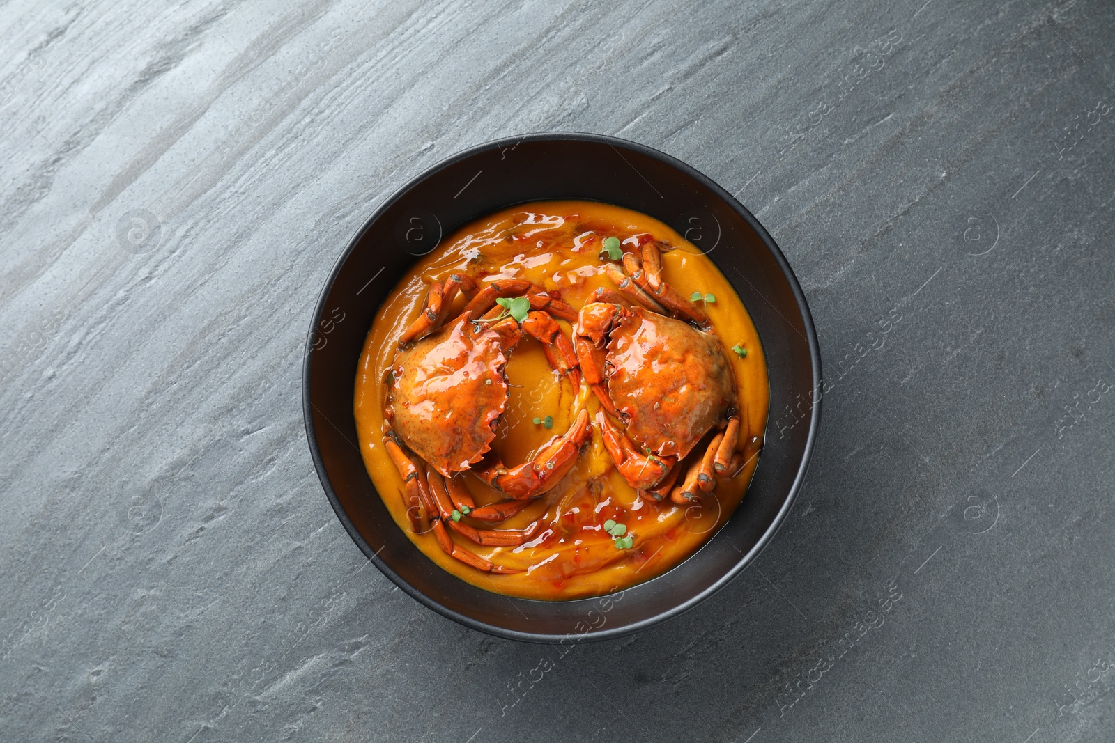 Photo of Delicious boiled crabs with sauce in bowl on grey textured table, top view