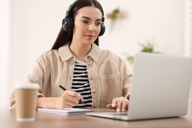 Young woman in headphones watching webinar at table in room