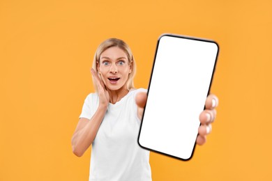 Surprised woman holding smartphone with blank screen on orange background