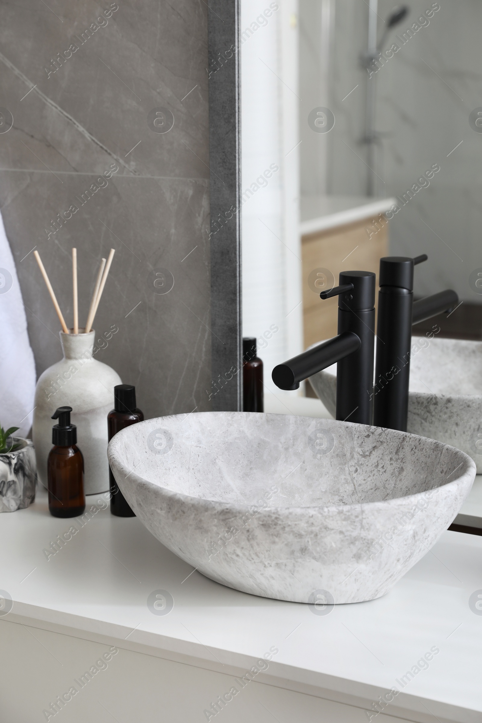 Photo of Stone vessel sink with faucet and toiletries on white countertop in bathroom