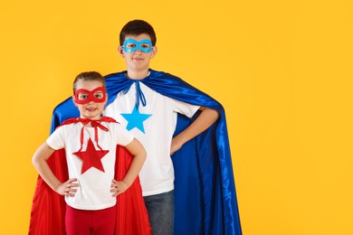 Photo of Boy and little girl in superhero costumes on yellow background. Space for text