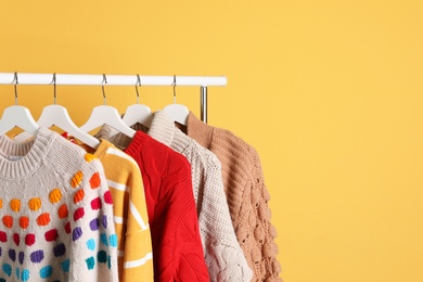 Collection of warm sweaters hanging on rack against color background. Space for text