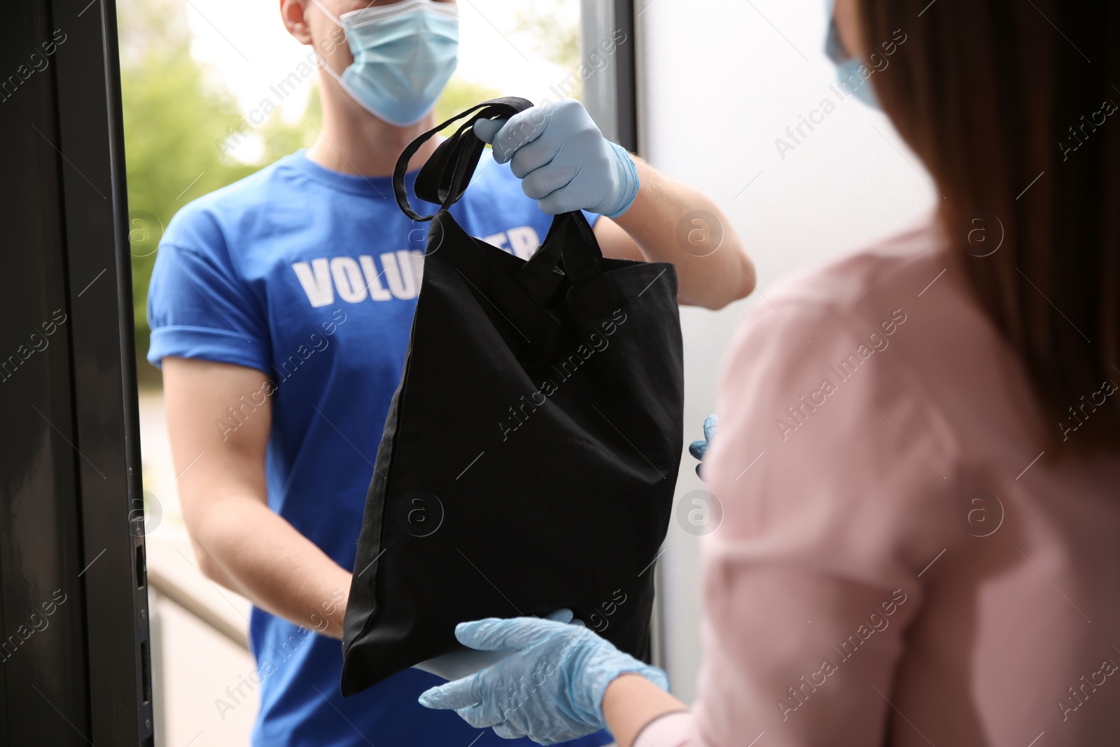Photo of Male volunteer giving black bag to woman through doorway, closeup. Aid during coronavirus quarantine