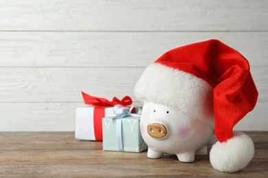 Photo of Piggy bank with Santa hat and gift boxes on wooden table. Space for text