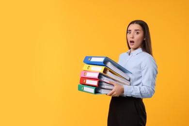 Shocked woman with folders on orange background, space for text