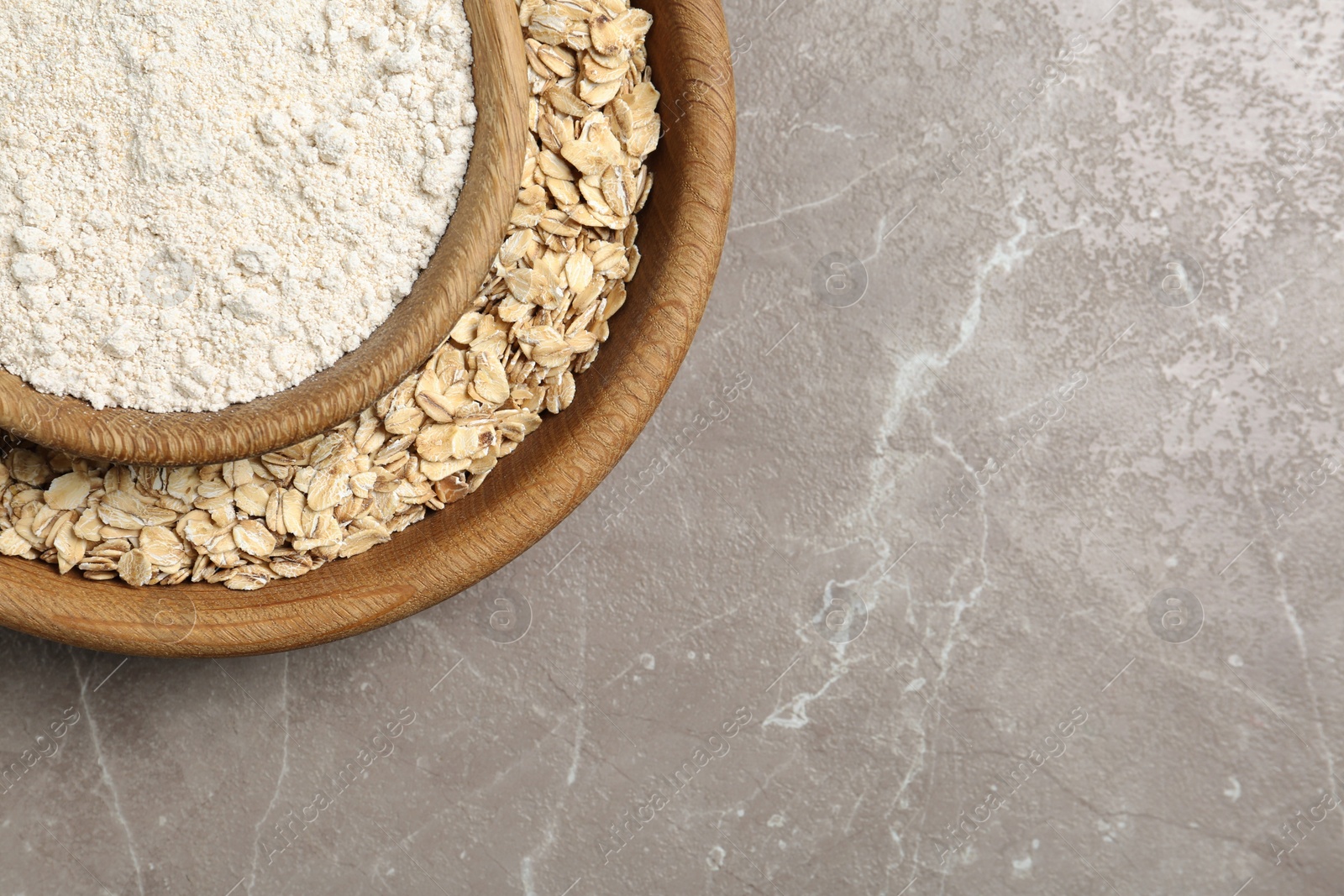 Photo of Bowls with oat flour and flakes on grey background, top view. Space for text