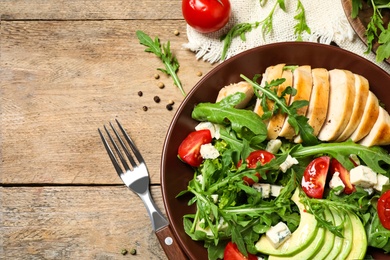 Photo of Delicious salad with chicken, arugula and avocado on wooden table, flat lay. Space for text