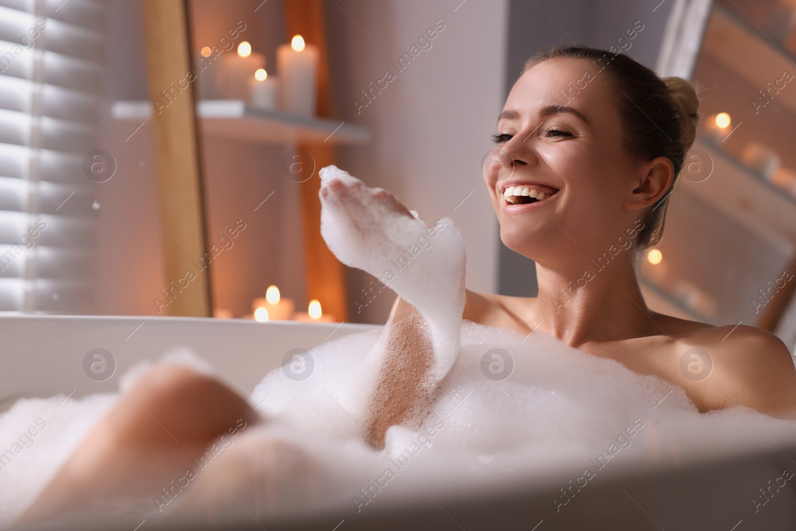 Photo of Beautiful woman taking bath in tub with foam indoors