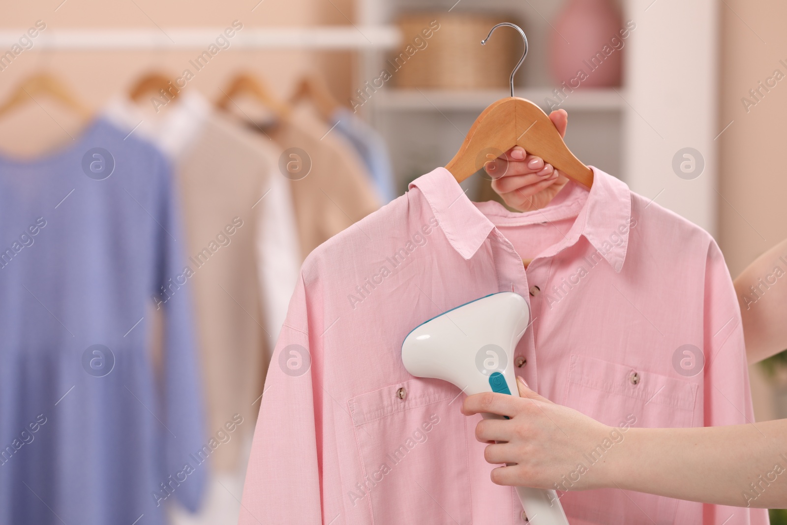 Photo of Woman steaming shirt on hanger at home, closeup