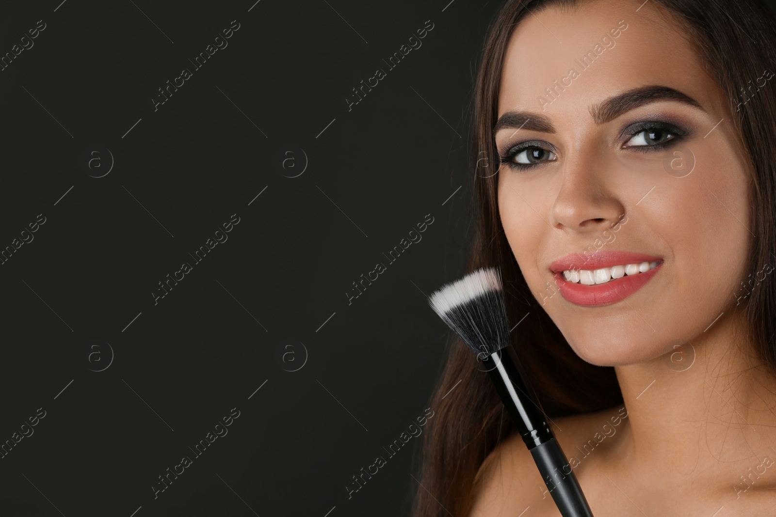 Photo of Portrait of beautiful woman with makeup brush on dark background. Space for text