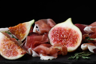Photo of Delicious ripe figs and prosciutto served on slate board, closeup