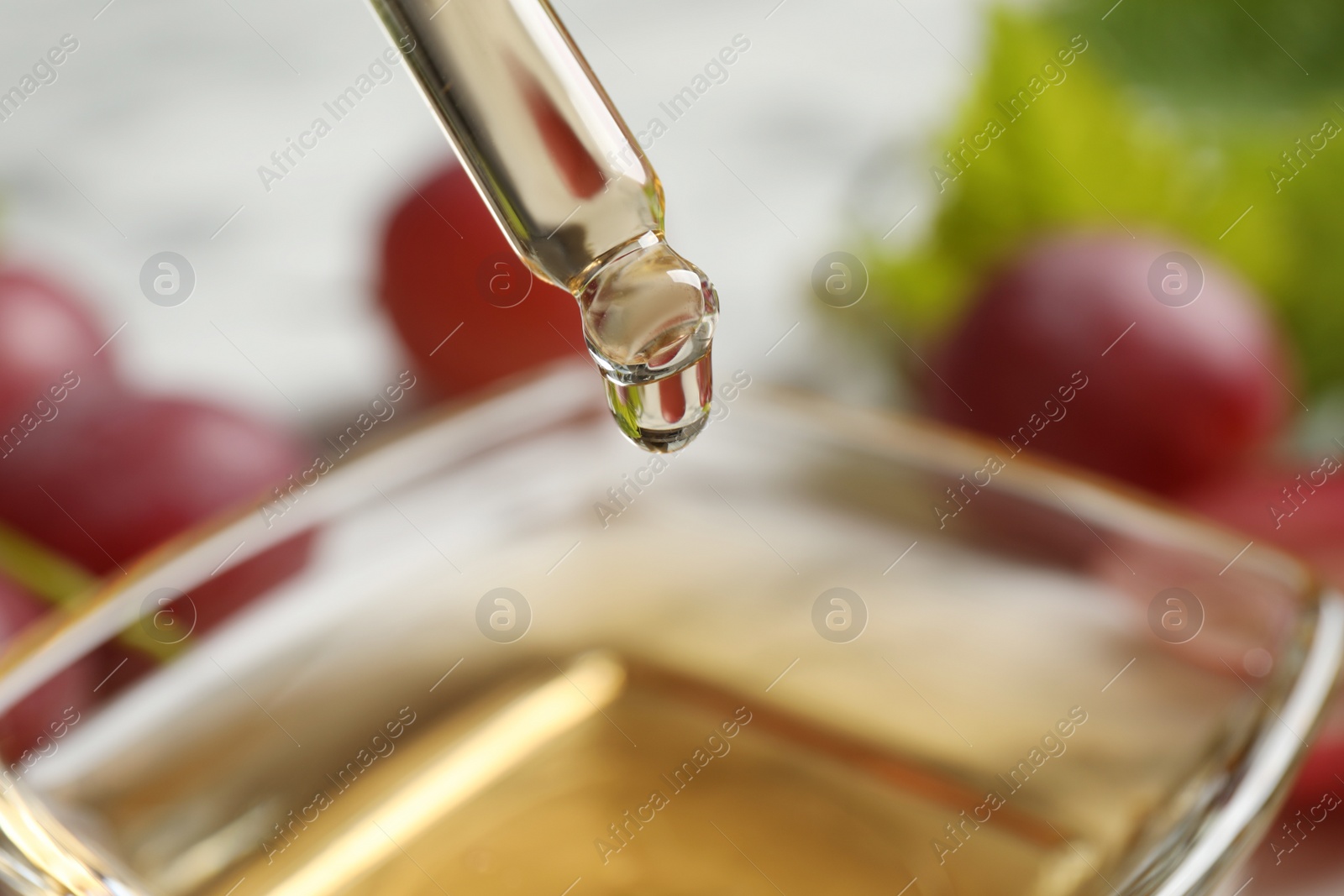 Photo of Dripping natural grape seed oil into bowl, closeup. Organic cosmetic