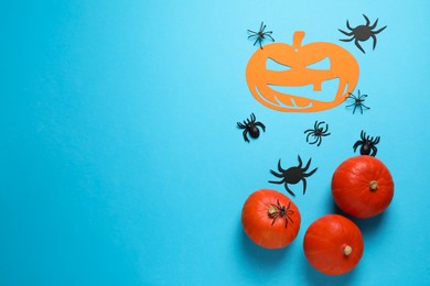 Photo of Flat lay composition with pumpkins and spiders on light blue background, space for text. Halloween celebration